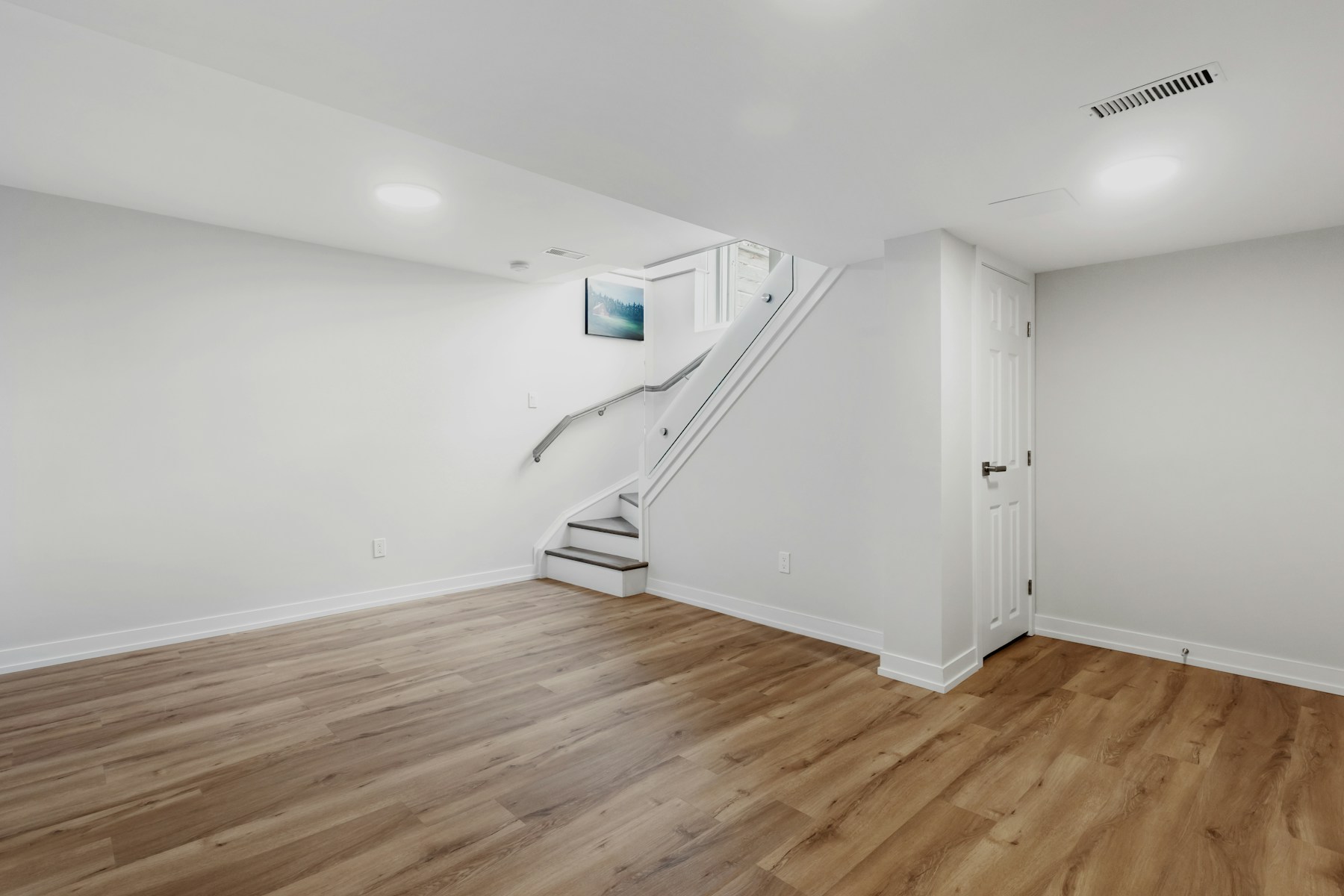 Bright finished basement with recessed lighting, white walls, and light wood-look flooring